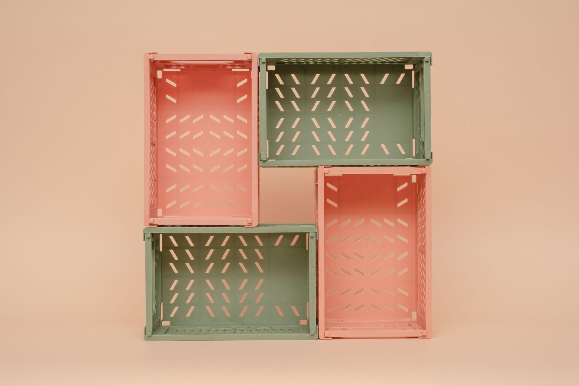 Four pink and green plastic foldable crates stacked on a beige background.