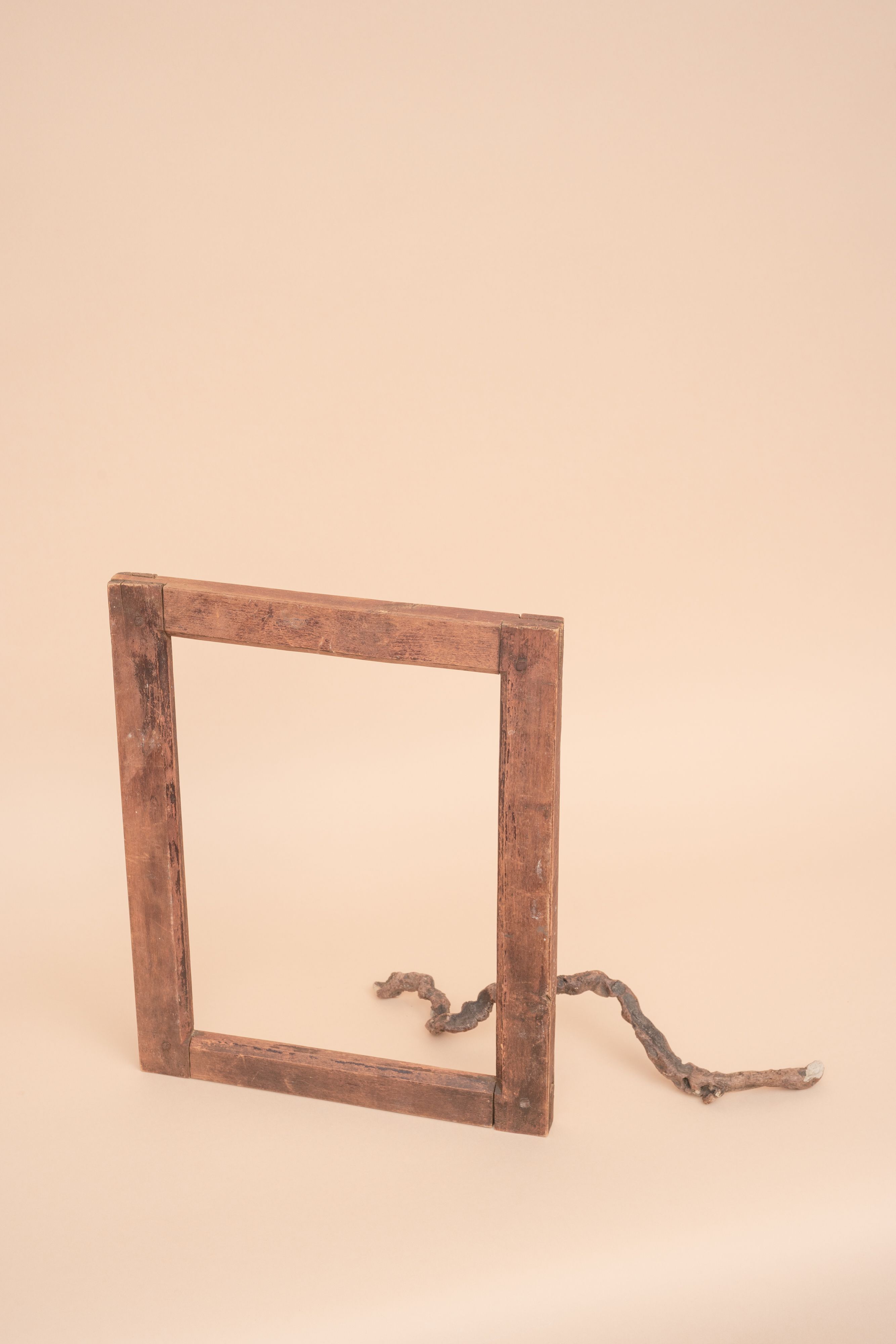 A rustic wooden frame and dry branch on a beige studio background, perfect for creative designs.