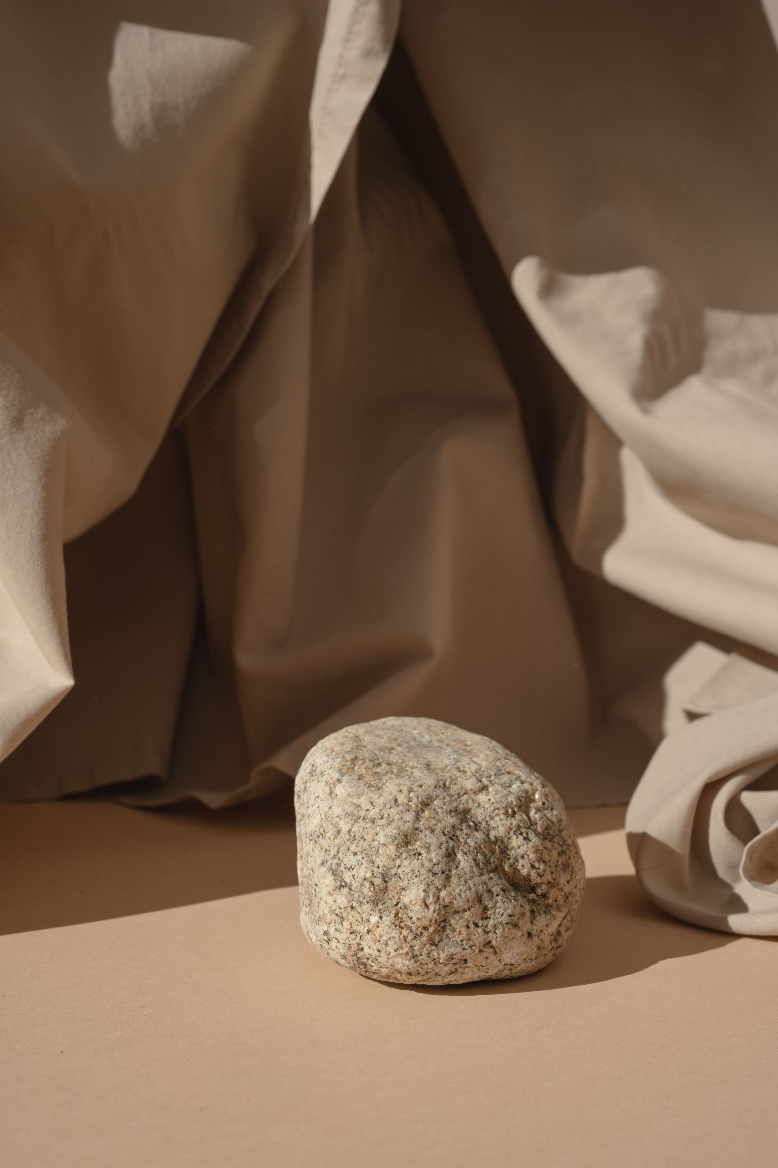 A textured stone on a beige fabric backdrop creating a minimalist still life composition.