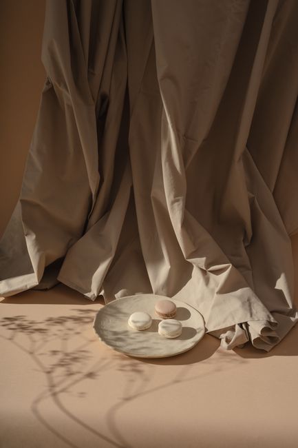 A minimalist still life featuring macarons on a plate with draped fabric backdrop in soft lighting.