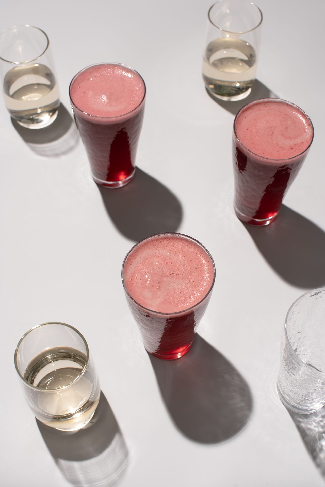 Close-up of assorted fresh fruit juices in glasses on a bright surface, casting soft shadows.