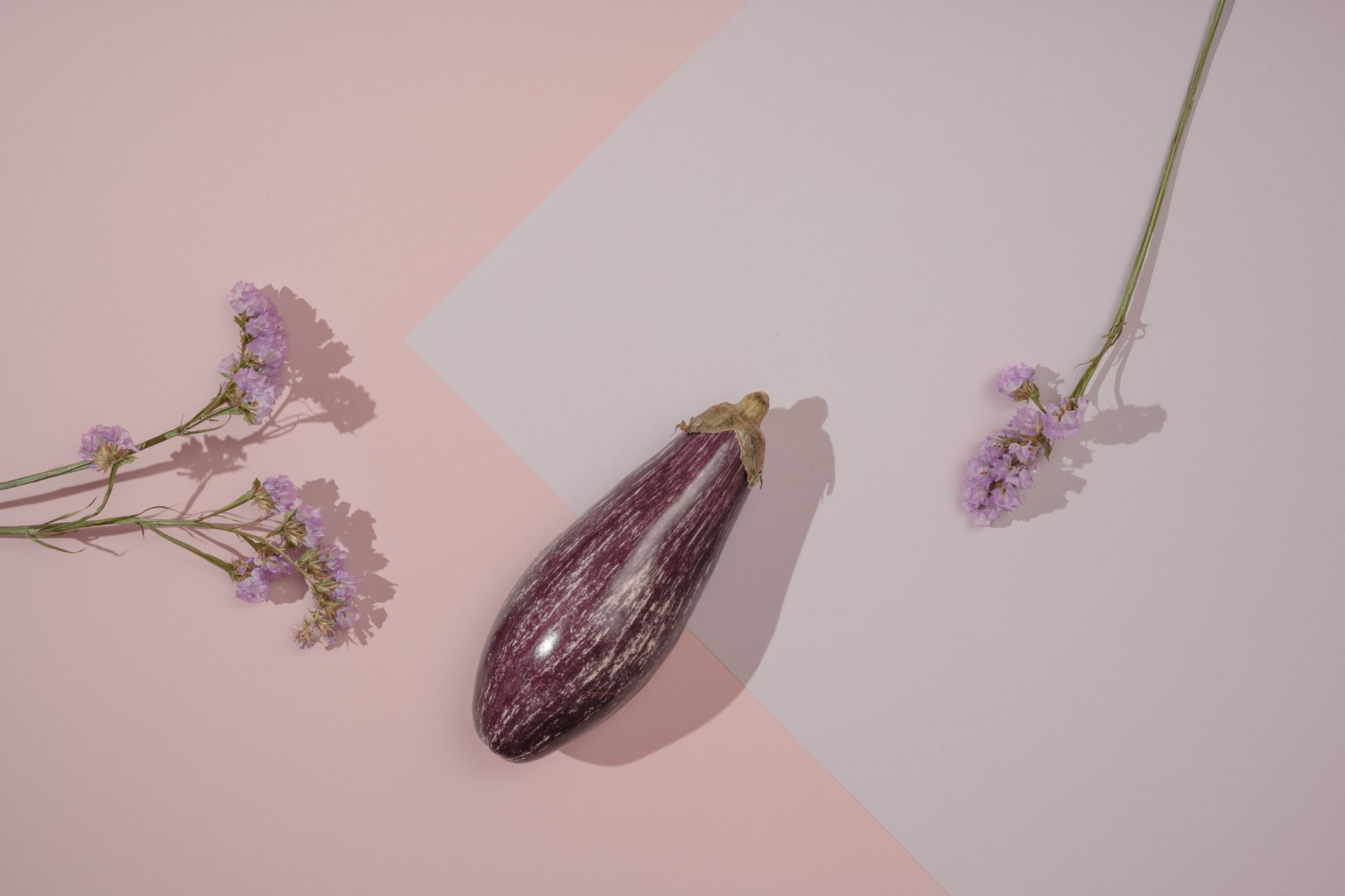 Artistic flat lay of purple eggplant with delicate pink flowers on a pastel background.