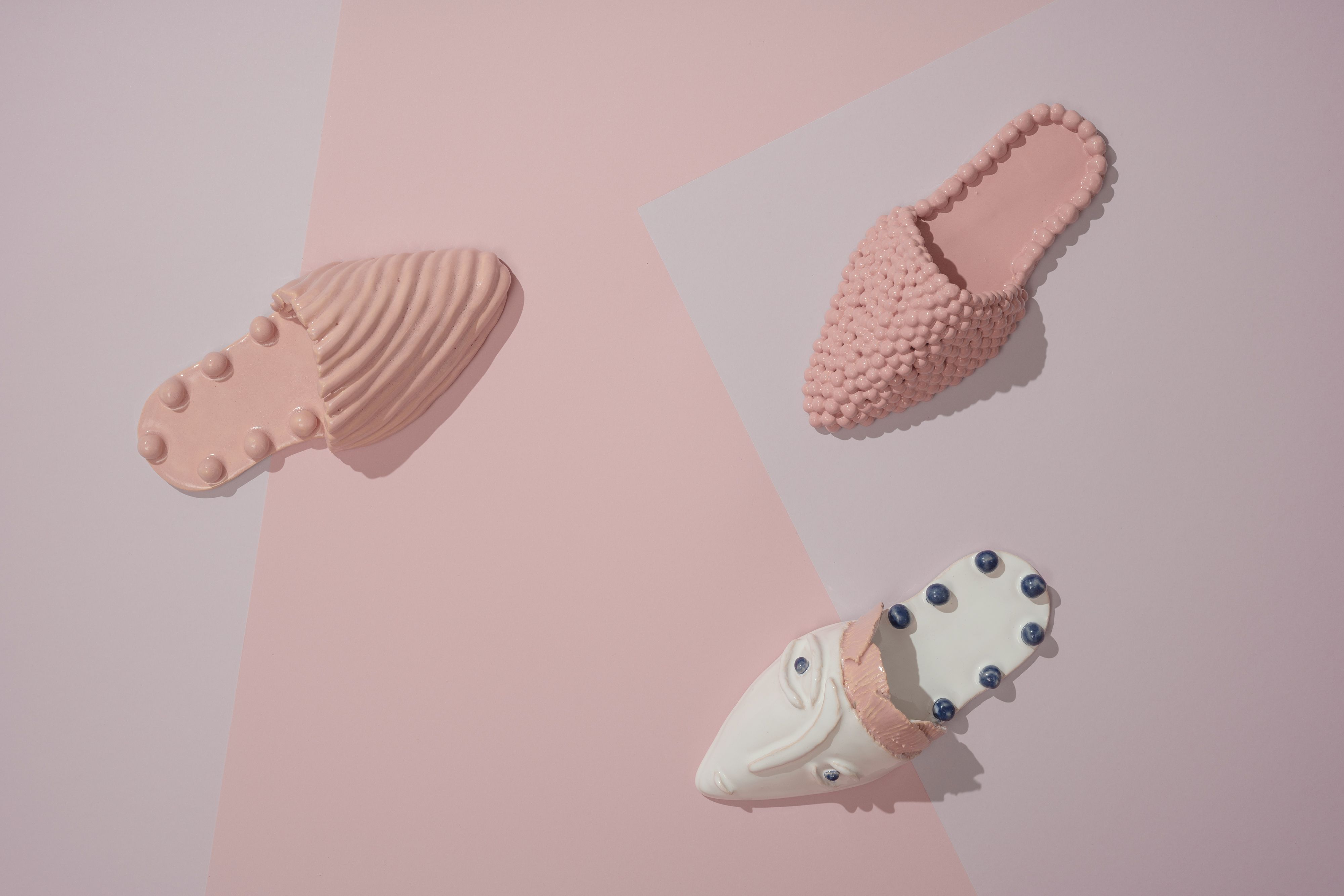 Creative display of ceramic slippers on a light pink geometric background, showcasing diverse textures.