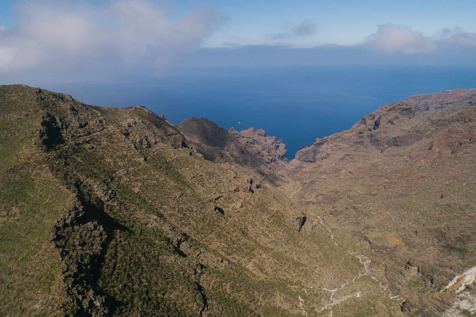 Dramatic aerial view of rugged mountains meeting the ocean under clear skies.