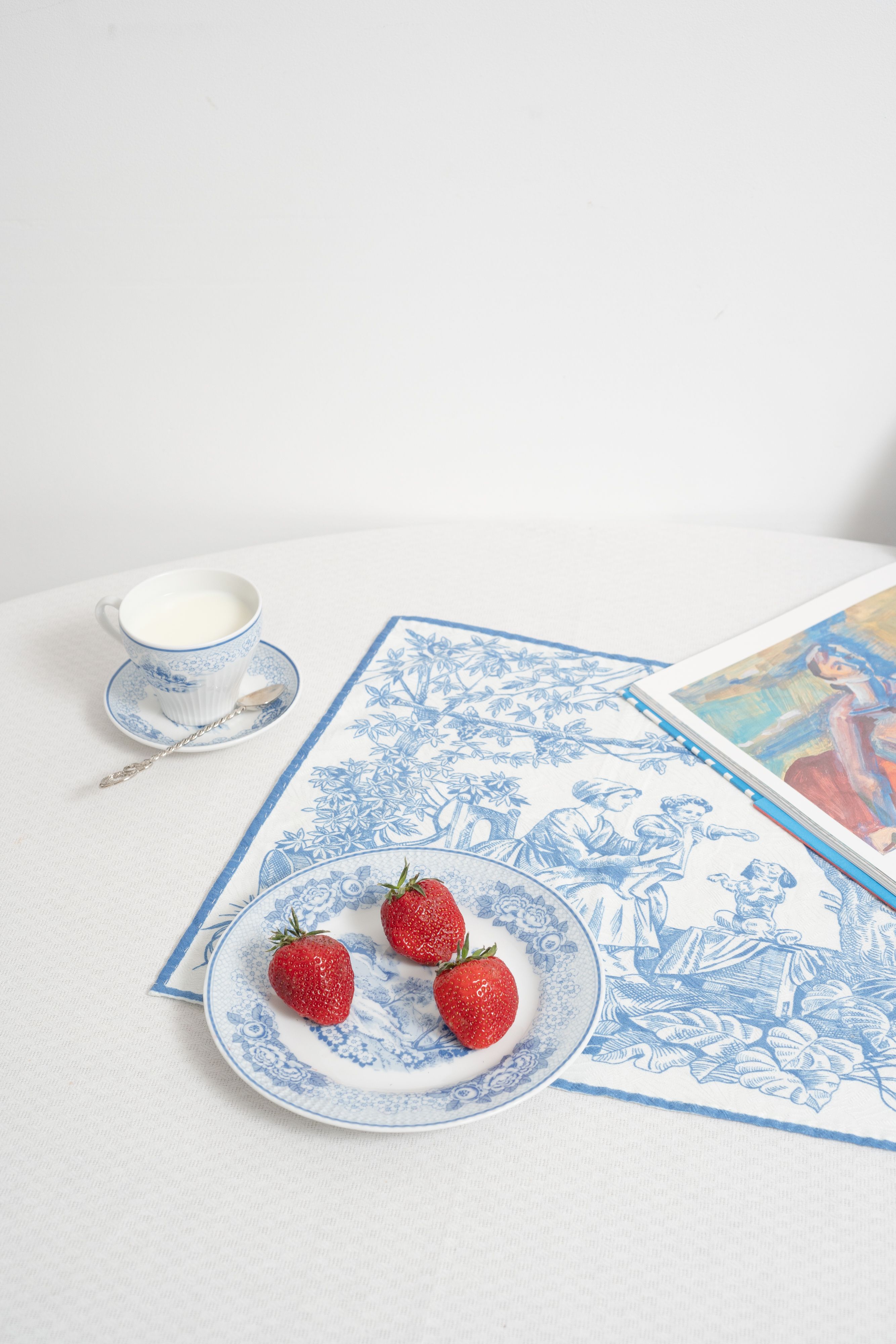 A classic table setup with strawberries, porcelain, and art book for a refined dining experience.