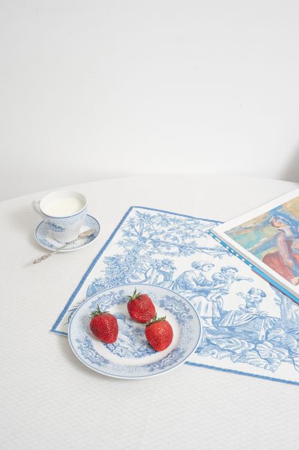 A classic table setup with strawberries, porcelain, and art book for a refined dining experience.
