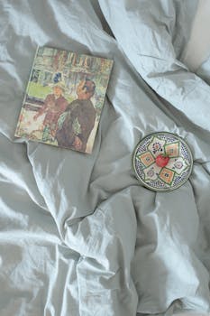 Book and decorative plate on bed with crumpled sheets, evoke a cozy morning ambiance.