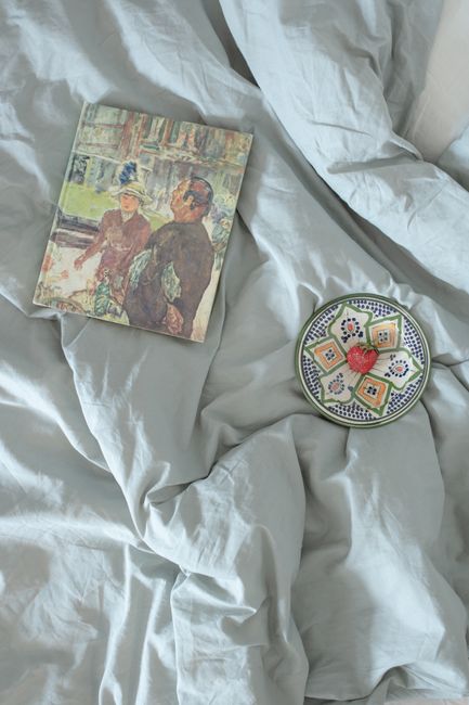 Book and decorative plate on bed with crumpled sheets, evoke a cozy morning ambiance.