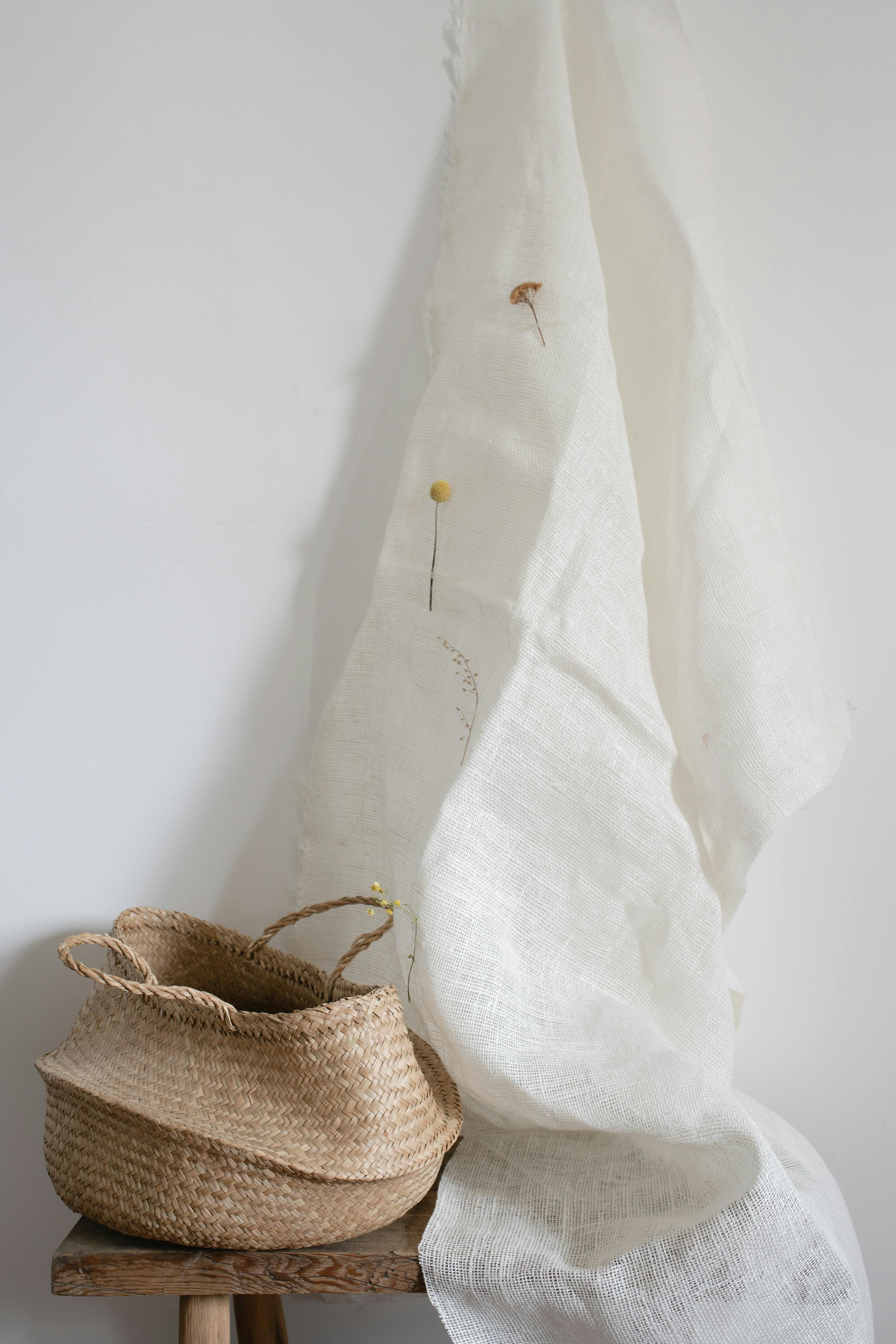 Elegant minimalist composition featuring a wicker basket and white draped fabric with subtle floral accents.