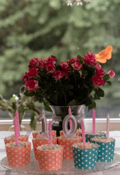 Polka dot cupcakes with candles and a rose bouquet create a festive scene.