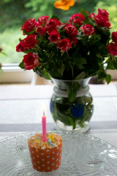 A charming birthday scene with a cupcake and lit candle, set beside a vase of vibrant red roses.