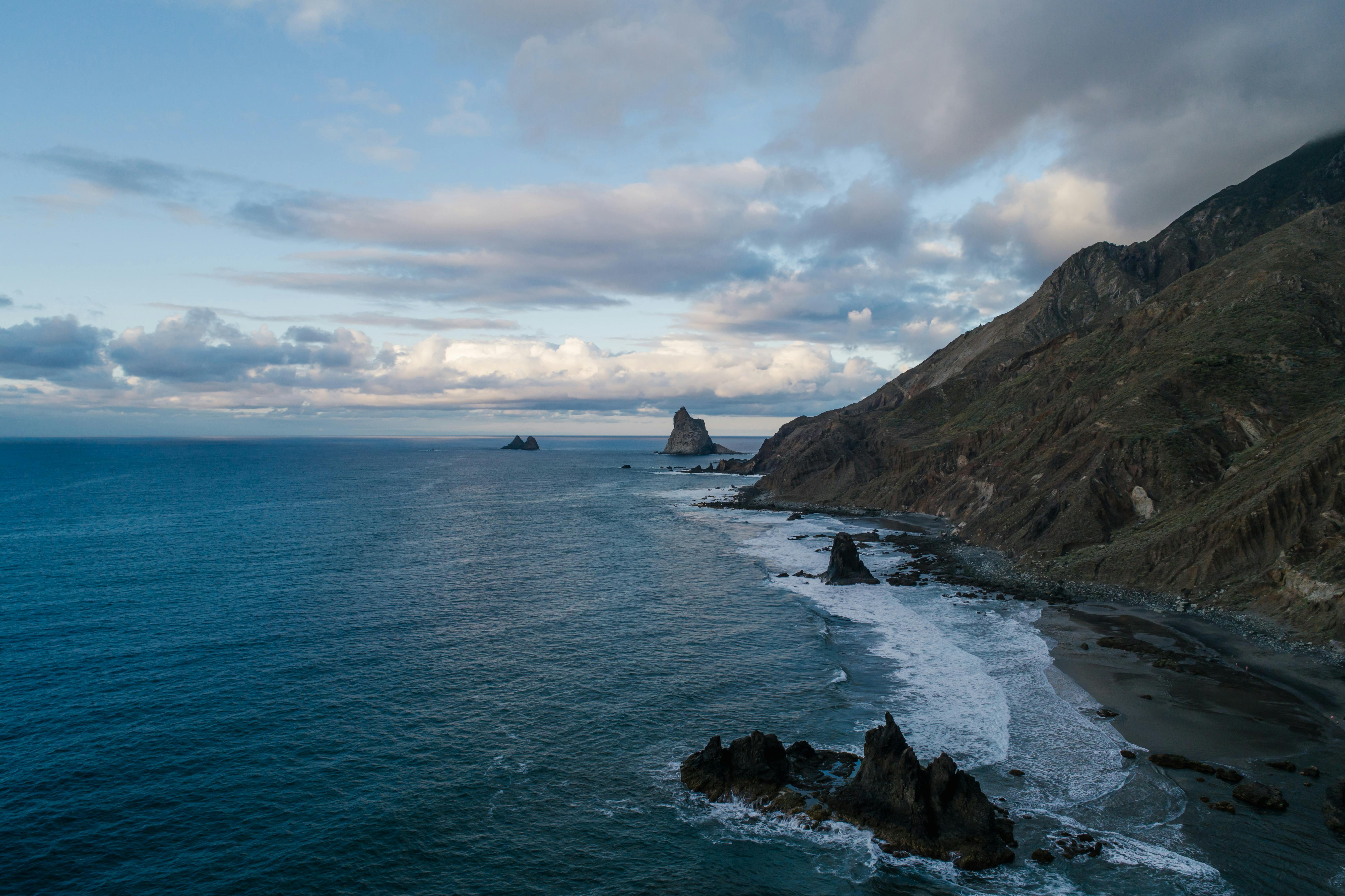 多云天空下，崎岖的海岸线、悬崖、海浪和蔚蓝的大海