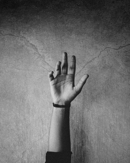 Free A close-up black and white image of a raised hand against a textured wall, evoking artistic expression. Stock Photo