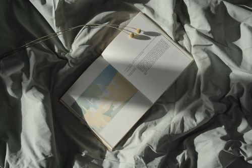 Free An open book rests on rumpled bed sheets, with sunlight casting soft shadows. Stock Photo