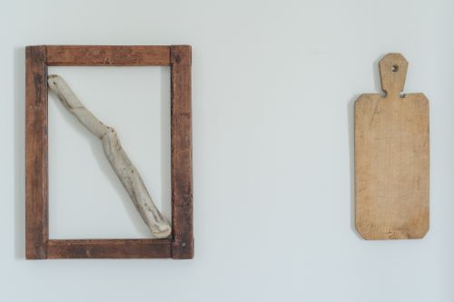 Free A minimalist composition featuring a rustic wooden frame with driftwood and a cutting board on a white wall. Stock Photo