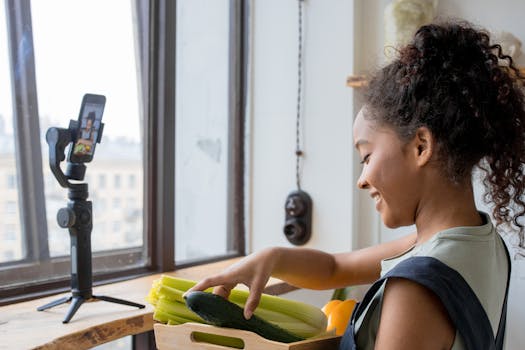 A woman arranges vegetables while recording a cooking video on her smartphone indoors.