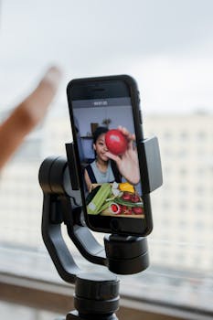 A vlogger uses a smartphone on a gimbal for recording a cooking vlog indoors.