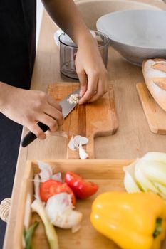 Close-up of hands slicing garlic and vegetables on wooden chopping board, fresh cooking ingredients.