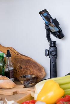 A smartphone mounted on a gimbal filming a kitchen cooking setup with vegetables.