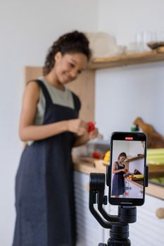 A woman prepares food in a kitchen while recording with a smartphone on a stabilizer.