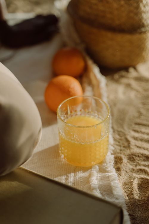 Free A close-up of a glass of fresh orange juice on a sandy beach picnic setup. Stock Photo