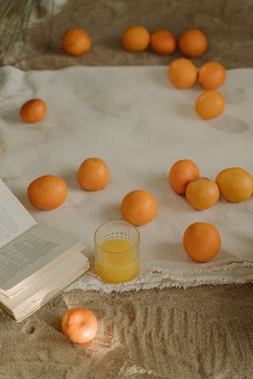 Free A serene beach picnic setup with fresh oranges and a glass of juice on a blanket. Stock Photo