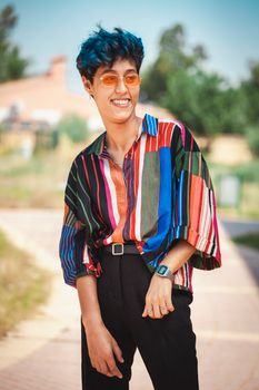 Stylish individual in a colorful shirt and sunglasses, smiling outdoors.