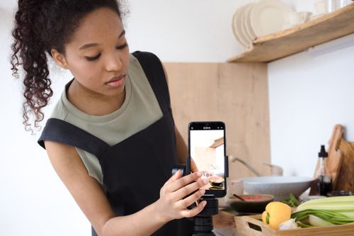 Free A young woman filming a cooking tutorial in her kitchen using a smartphone. Stock Photo