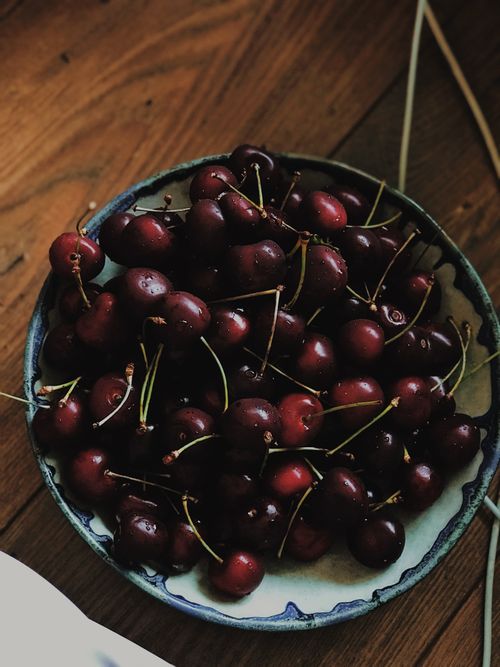 Free Top view of a bowl filled with ripe cherries on a wooden table, capturing organic freshness. Stock Photo
