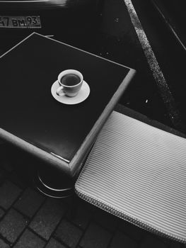 A black and white photo of a coffee cup on an outdoor table, evoking a retro ambiance.
