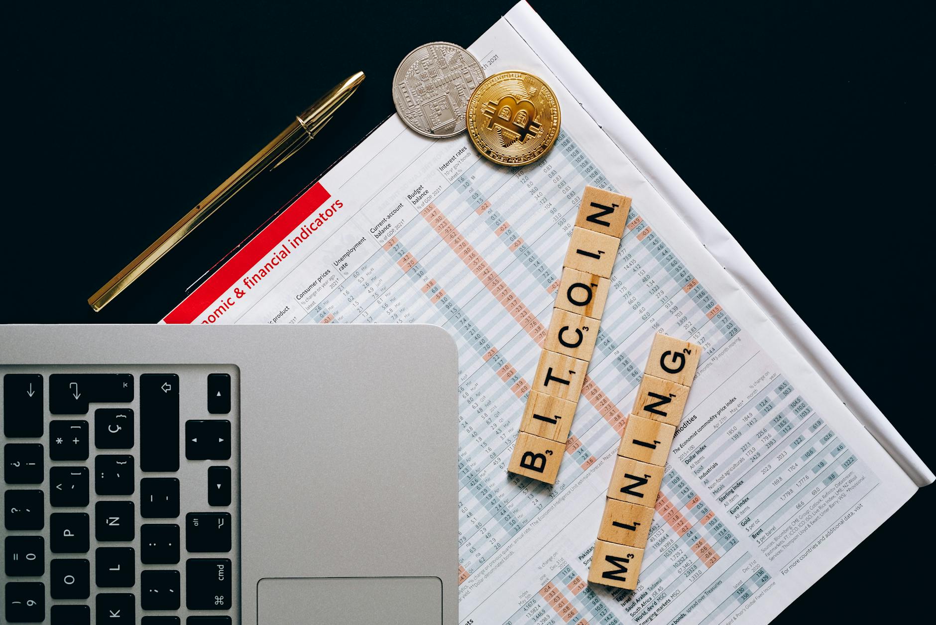Top view of a laptop, Bitcoin coins, and financial indicators symbolizing Bitcoin mining and investment.
