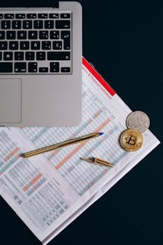 Top view of financial documents, laptop, and cryptocurrency coins on a desk.