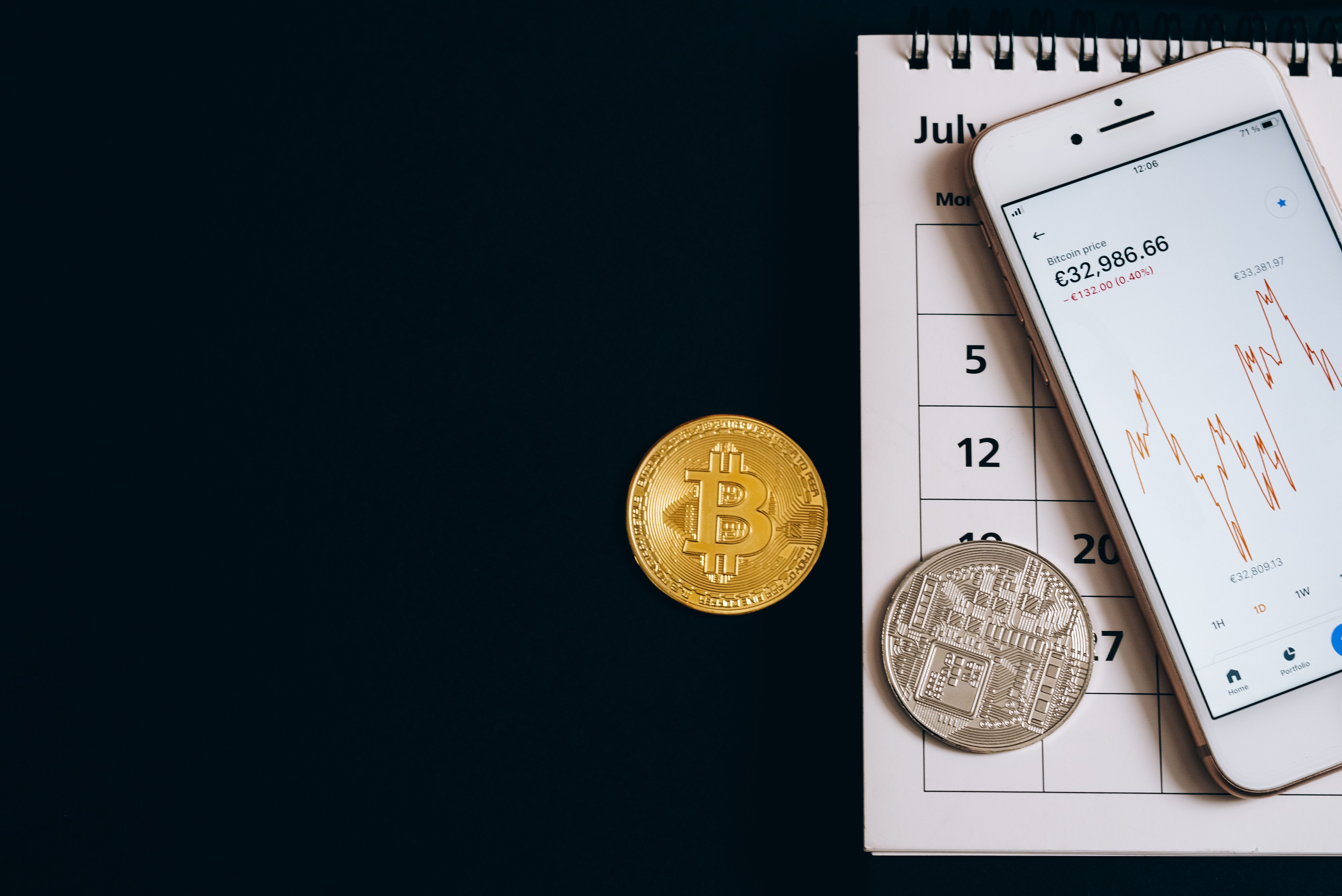 Bitcoin coins on a calendar with a smartphone showing price trends, illustrating finance dynamics.