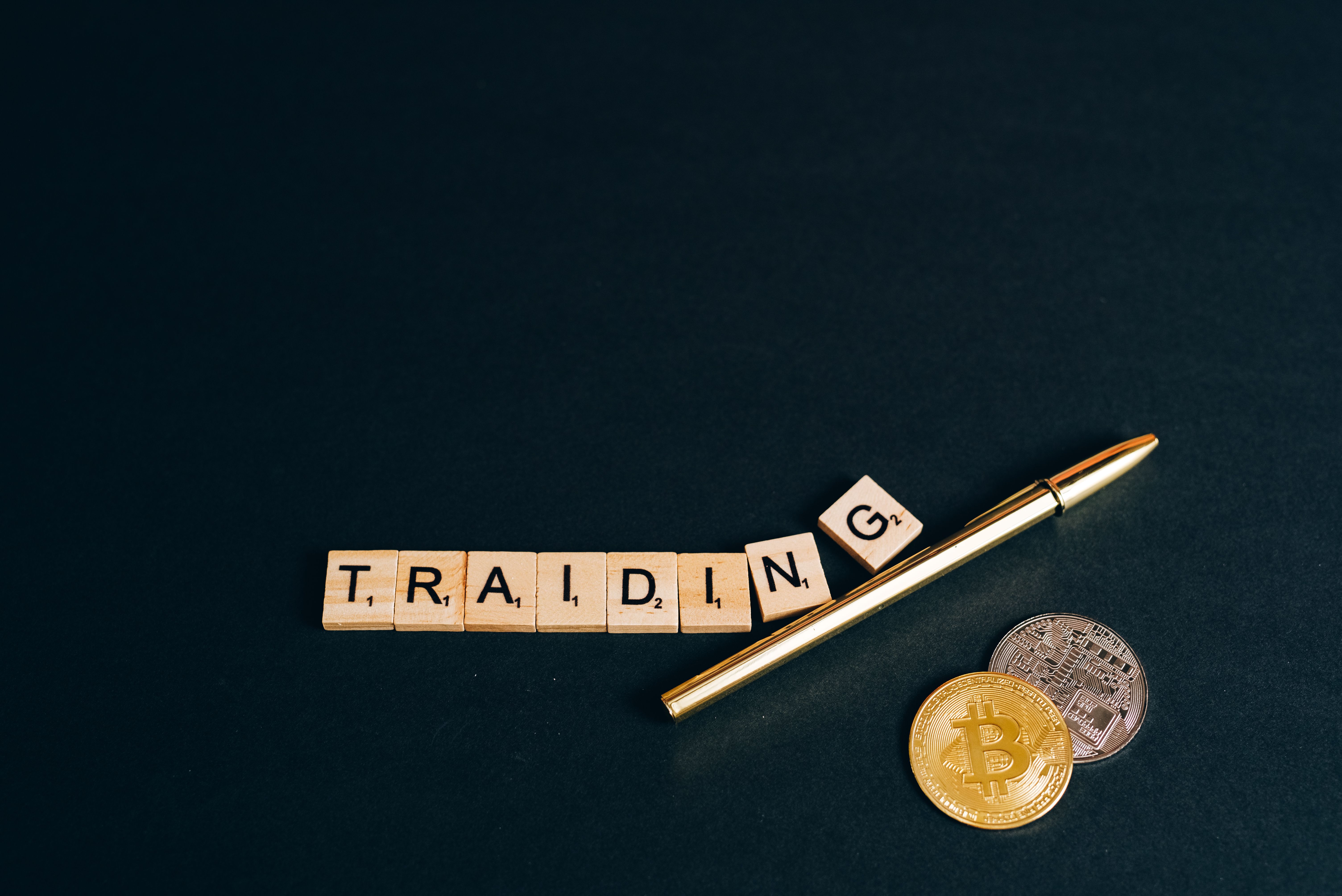 Bitcoin and trading concept shown with coins, pen, and letter tiles on a dark background.