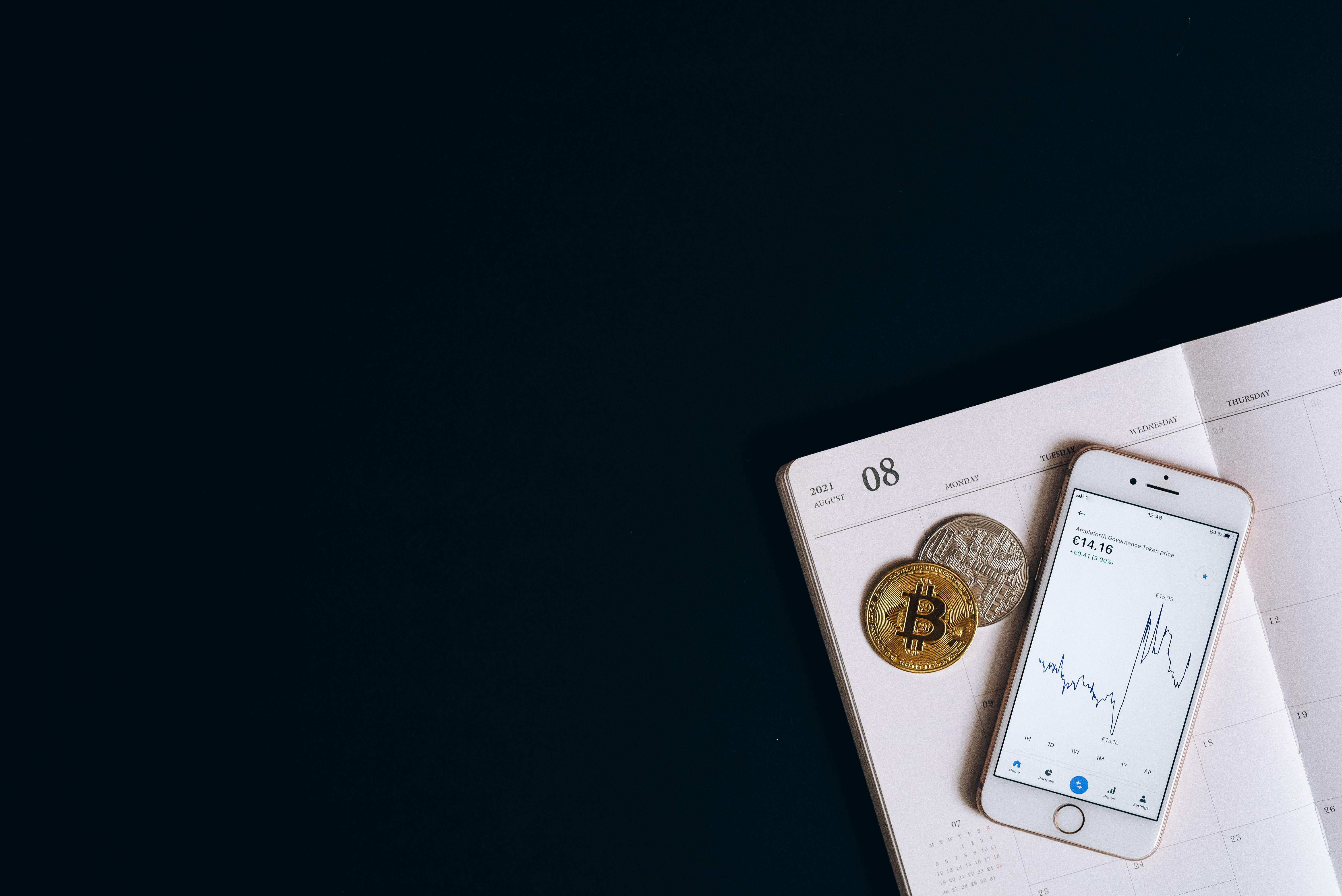 Smartphone displaying cryptocurrency data next to Bitcoin on a calendar offers finance and technology insights.