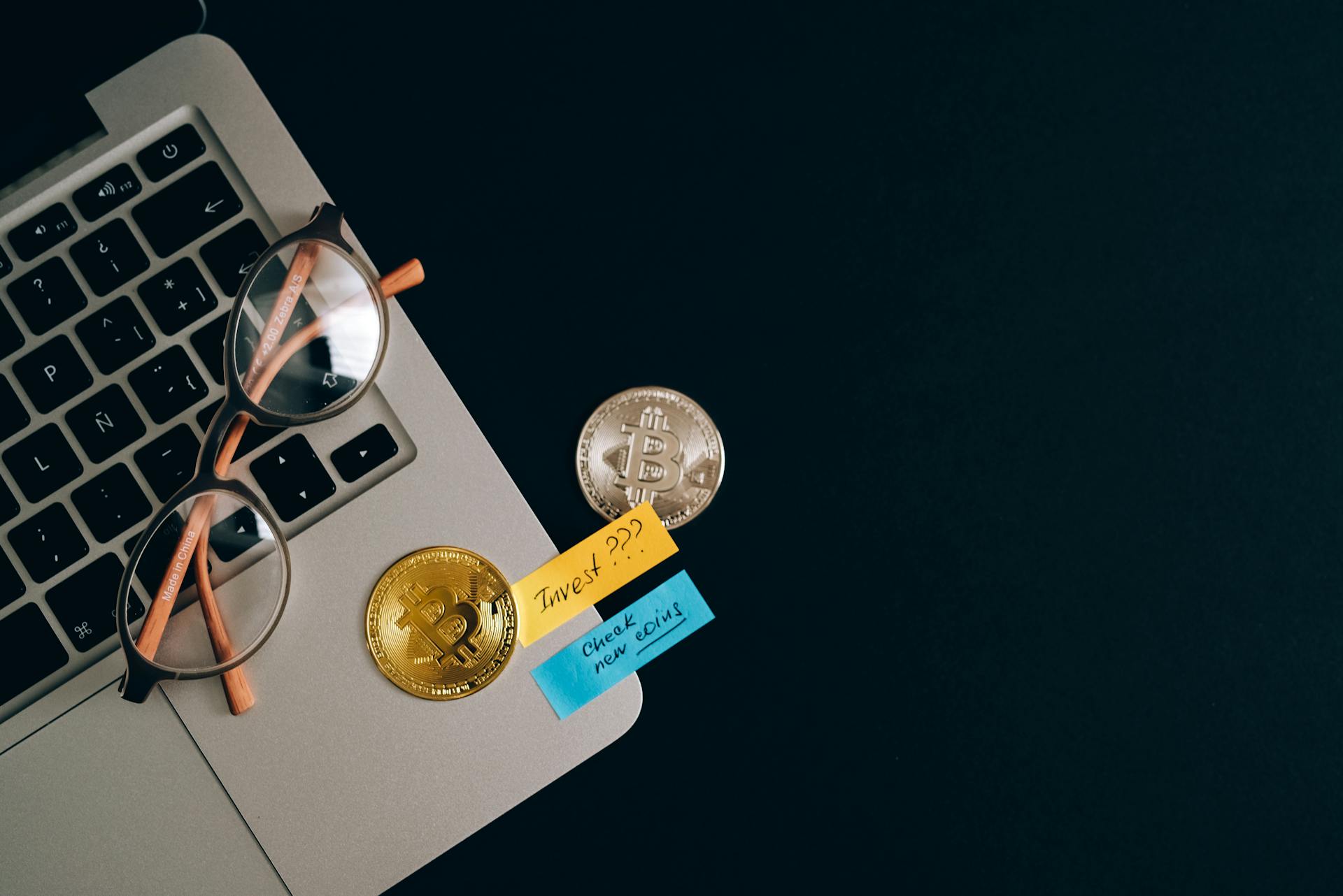 Laptop, bitcoins, and notes on a desk representing cryptocurrency investment concept.