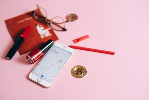 White Smartphone Beside Gold Bitcoin on Pink Surface