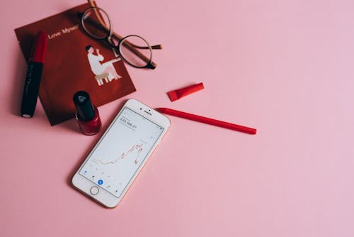 White Smartphone Beside Eyeglasses on Pink Surface