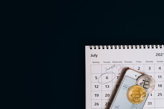Top view of bitcoins and smartphone on July 2021 calendar, suggesting investment planning.