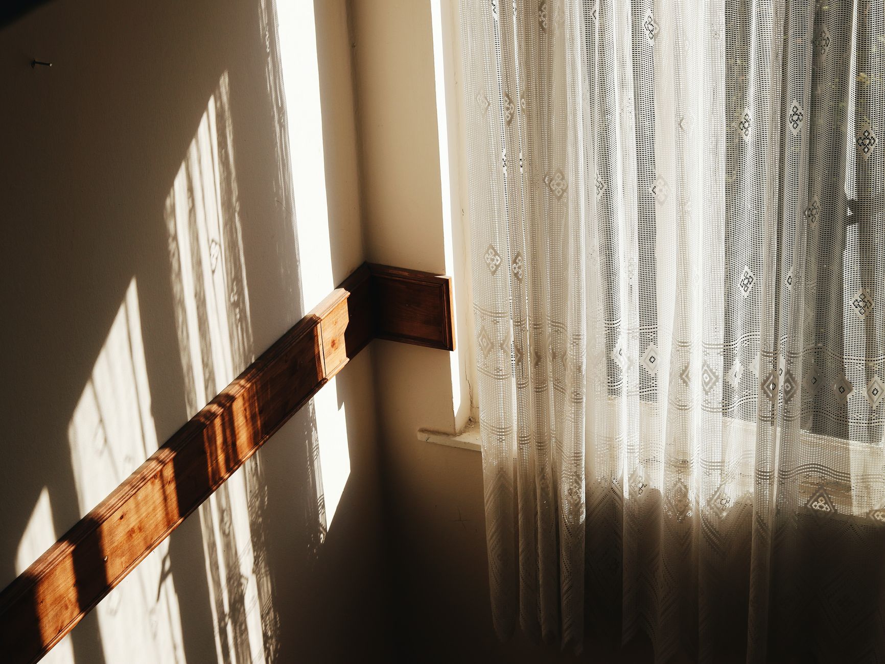 Tranquil scene of sunlight casting soft shadows through a lace curtain in a cozy room corner.