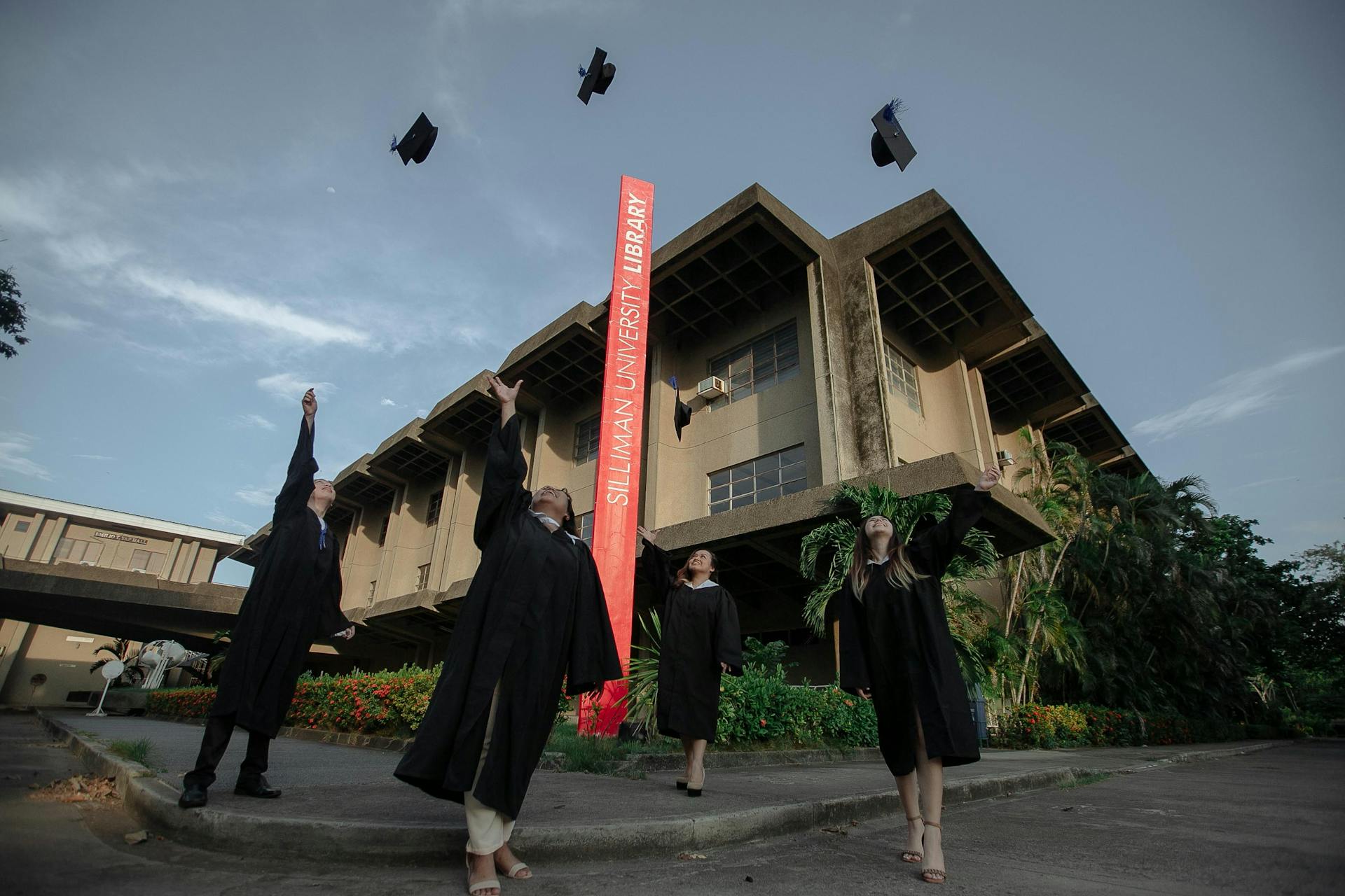 Graduates celebrate by throwing hats in front of Silliman University Library, showcasing academic success.