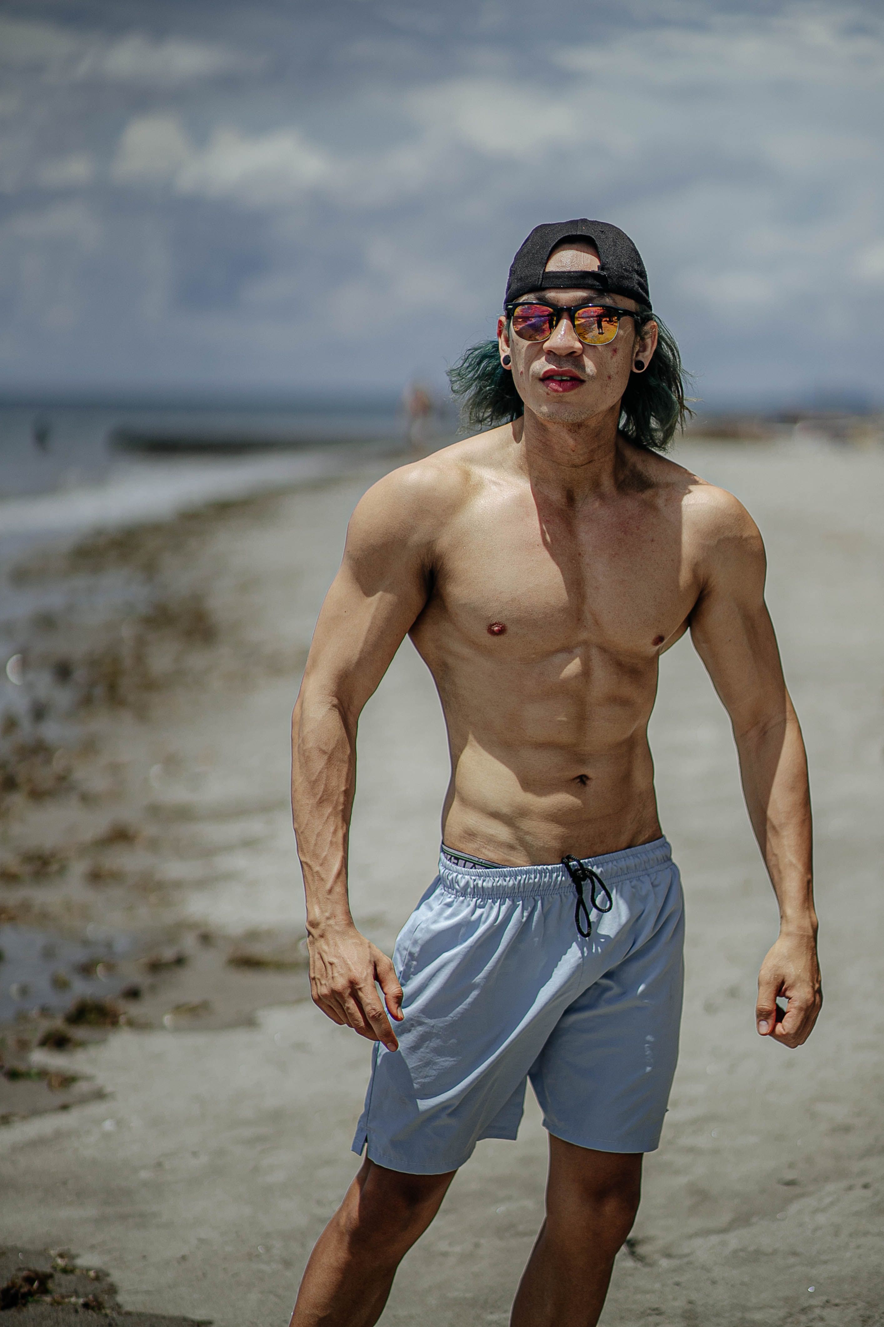 Fit adult male with muscular build posing on a beach under the sunny sky, embodying fitness and confidence.