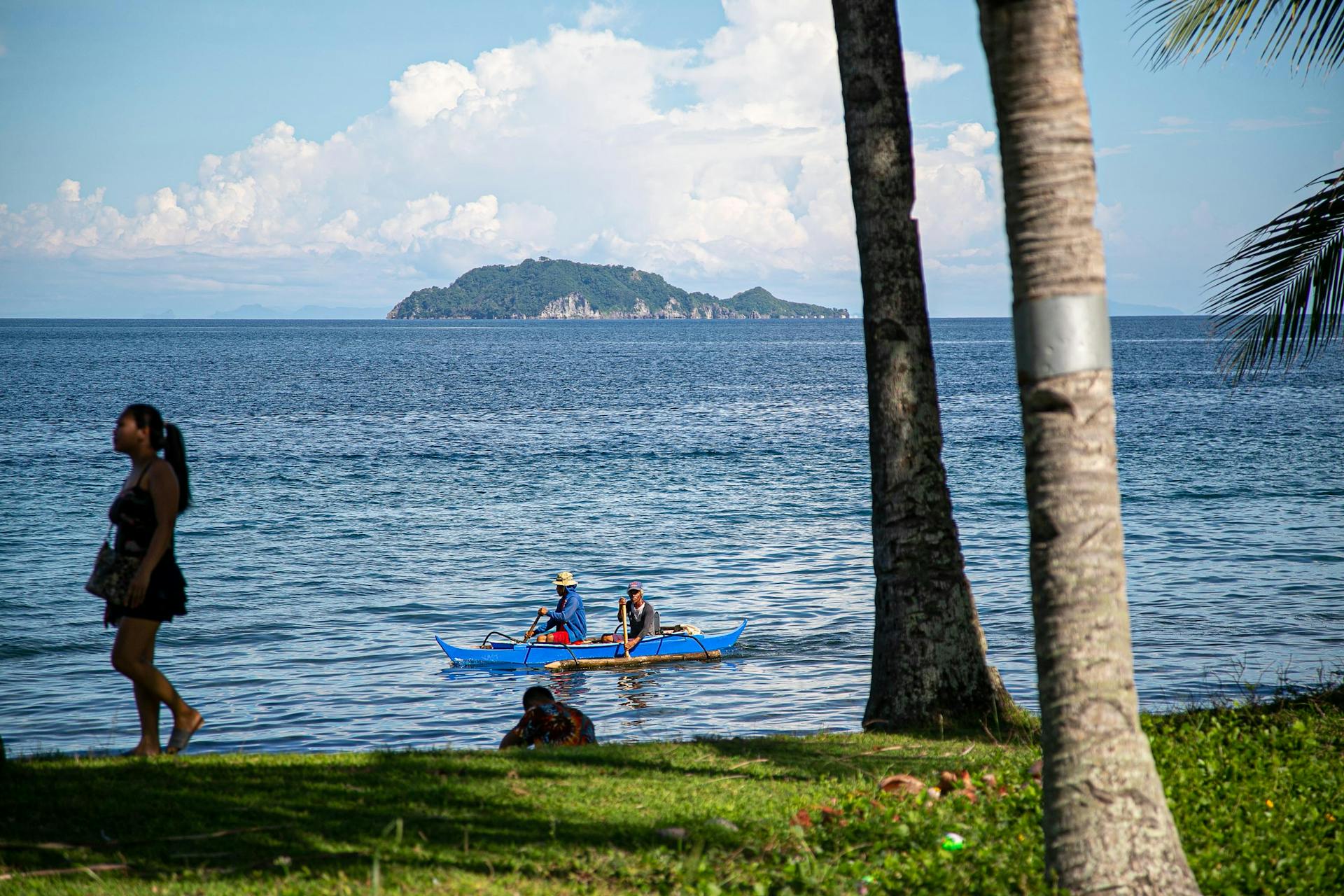 A serene beach setting in Dauin, Philippines, featuring people and a traditional boat against a stunning ocean backdrop.