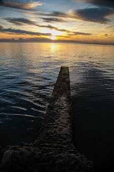 Sunset over calm sea with a concrete pier, perfect mobile wallpaper.