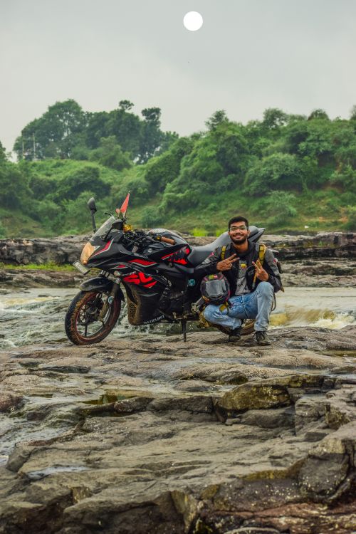 Free Man poses with motorcycle on rocky landscape under a cloudy sky, showcasing adventure travel. Stock Photo