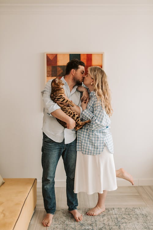 Man Holding a Cat While Kissing a Pregnant Woman