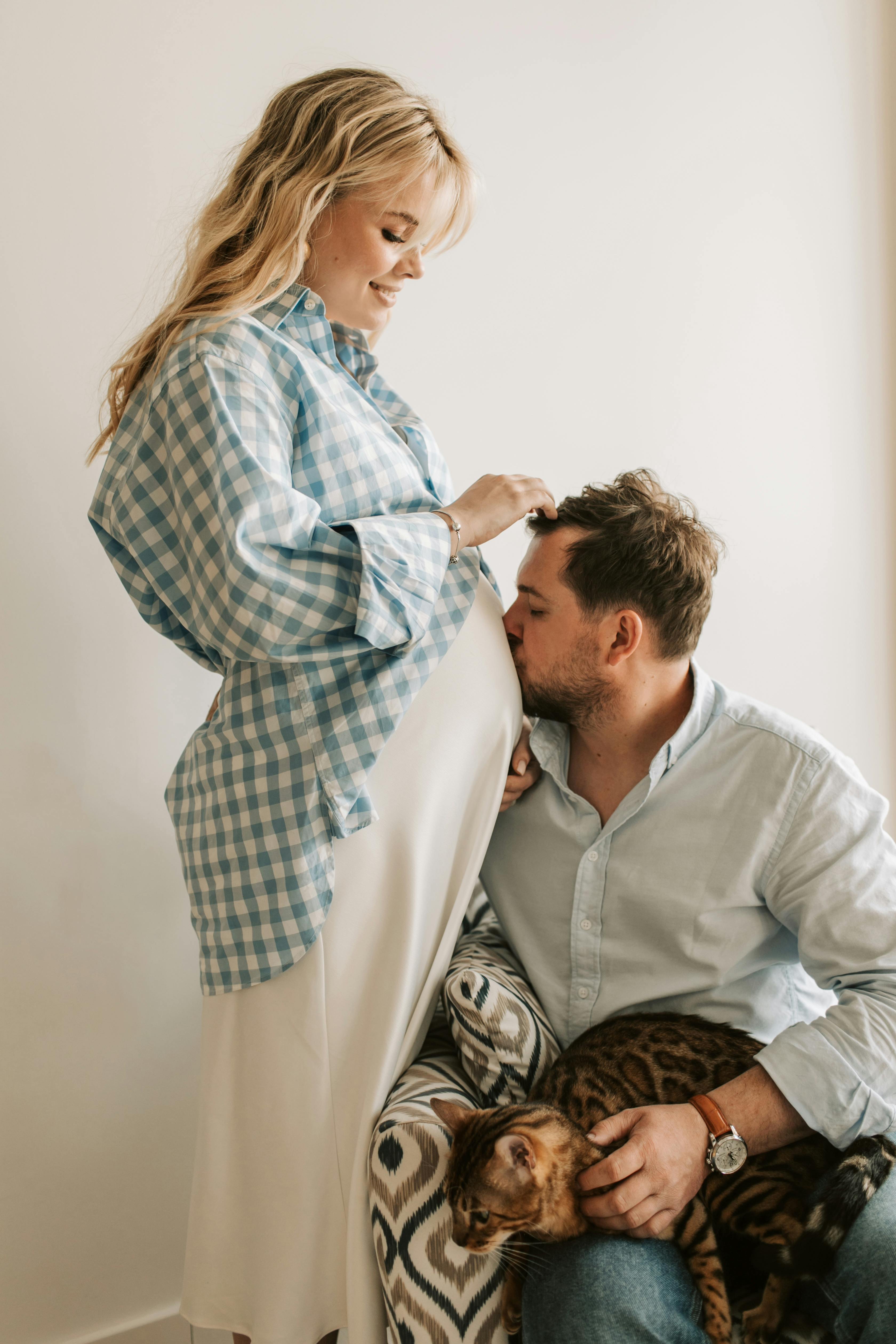 man kissing the baby belly of his wife and holding a cat