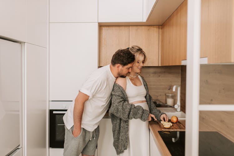 Man Leaning On The Shoulder Of A Woman Slicing An Apple