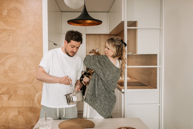 A Couple Cooking While Holding A Cat