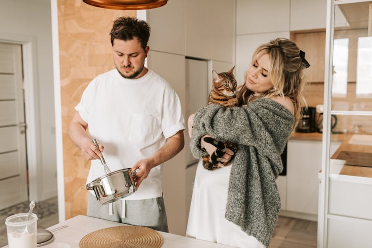 A Couple Cooking While Holding A Cat